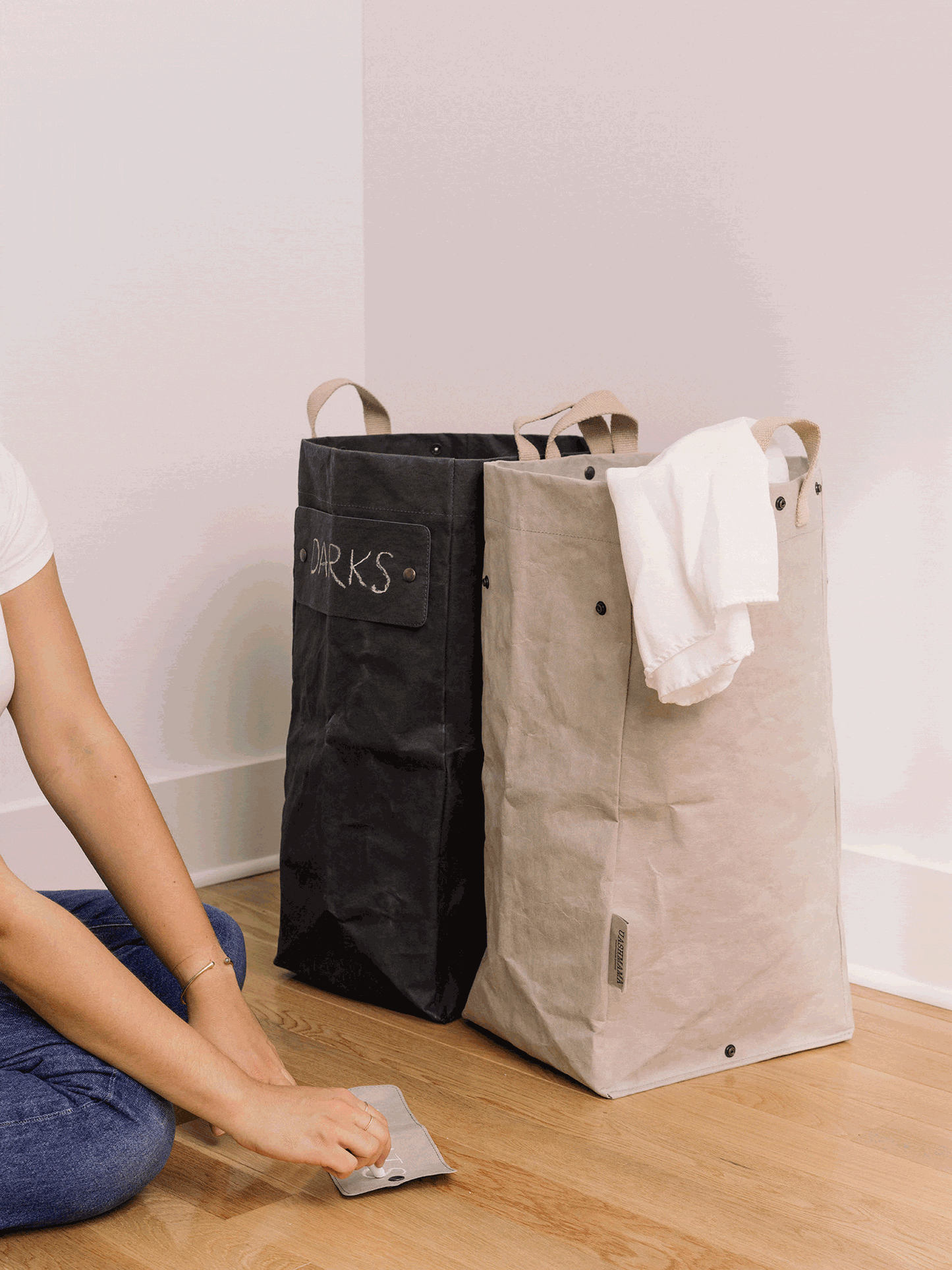 A GIF shows a woman labelling her washable paper laundry bags. The one at left is labelled "darks" and is black, and the one at right is grey and labelled "lights."
