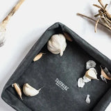 A black washable paper tray is shown from a top-down angle, containing cloves of garlic and a whole bulb.