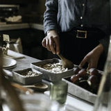 A woman serves nuts from a grey washable paper tray in a kitchen setting. 