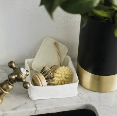 A grey washable paper tray sits atop a marble sink, containing dish brushes. 