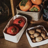 A set of three washable paper trays in grey sit on a wooden table. All in varying sizes, they contain pomegranates and walnuts.