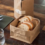 A washable paper tray in tan is shown containing sliced bread. A washable paper cooler in the same tone sits at rear, containing a water bottle.