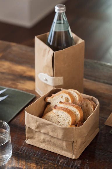 A washable paper tray in tan is shown containing sliced bread. A washable paper cooler in the same tone sits at rear, containing a water bottle.