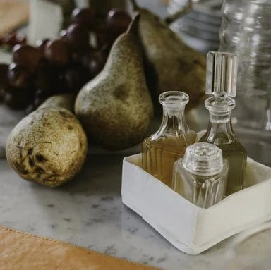 A washable paper tray in white is shown containing oils. It is in a tabletop setting next to three pears.