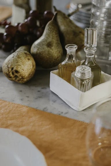 A washable paper tray in white is shown containing oils. It is in a tabletop setting next to three pears.