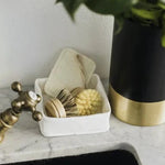 A grey washable paper tray sits atop a marble sink, containing dish brushes.