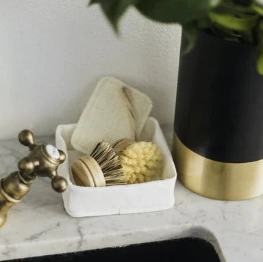 A grey washable paper tray sits atop a marble sink, containing dish brushes.