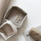 Two washable paper trays lie one on top of the other. The top one is small and cream, the bottom one is larger and contains jewellery. A washable paper key holder sits at right on top of a book. 