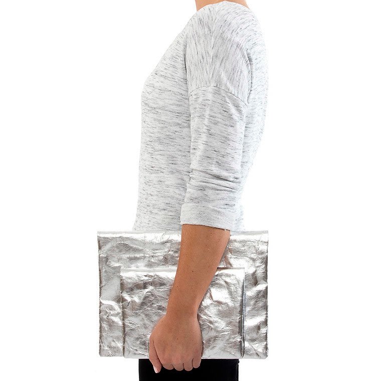 A person is shown holding two metallic silver washable paper clutches - one large and one small.