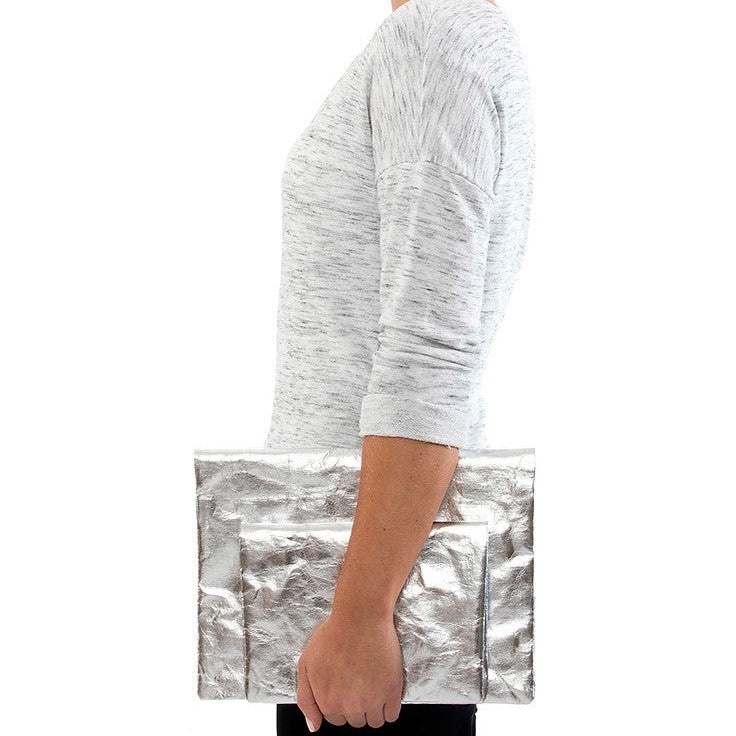 A person is shown holding two shiny metallic silver washable paper clutches - one large and one small.