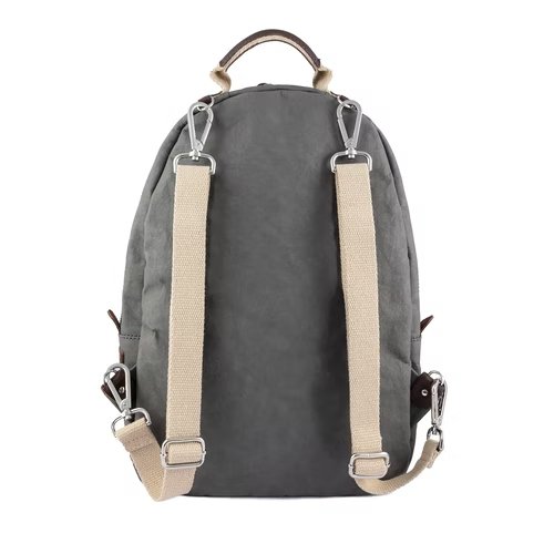 A grey washable paper backpack is shown from the back angle. It is oval in shape, has a top handle, two cream canvas straps, and silver hardware.