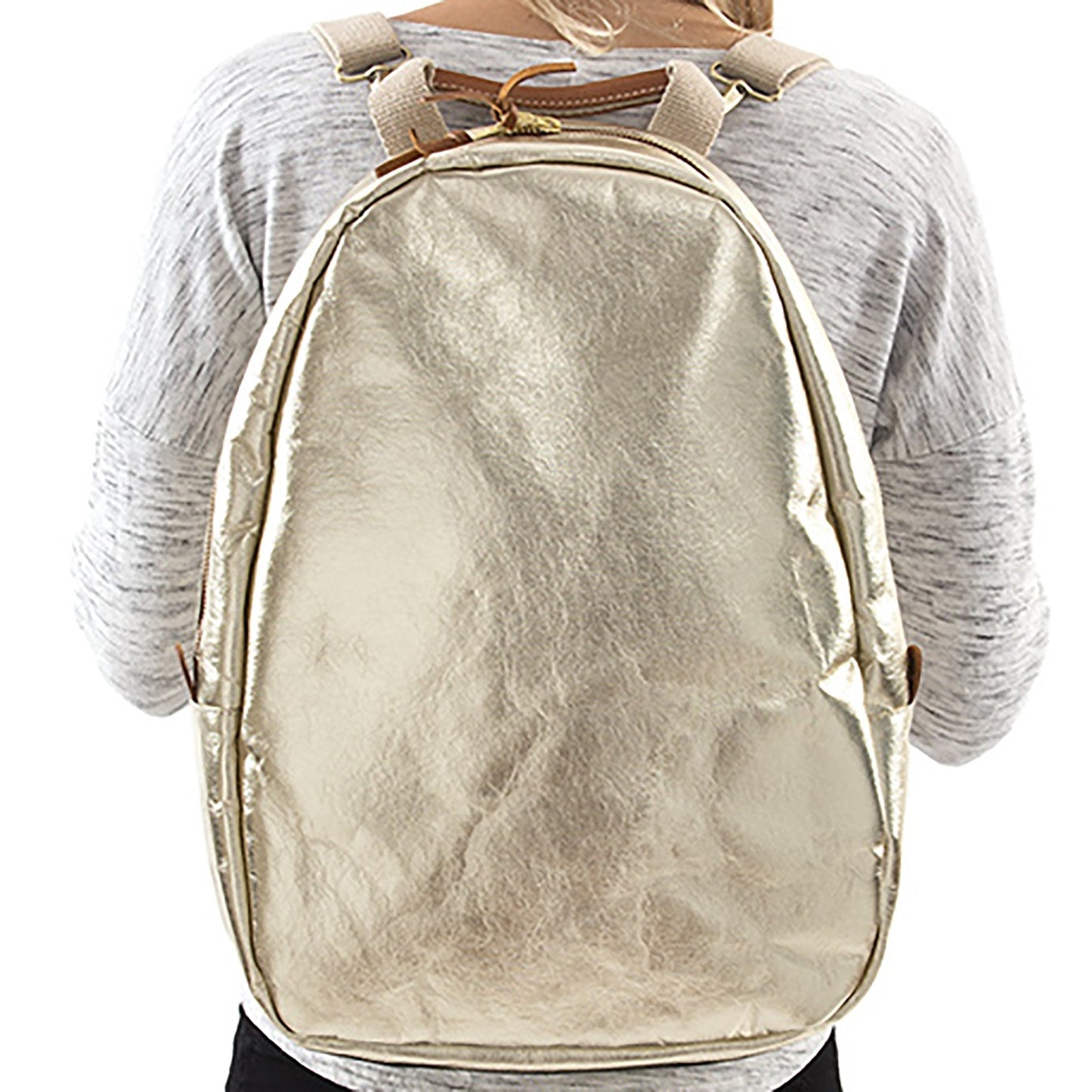 A blonde woman is shown wearing a washable paper backpack. It has two side zip toggles, is oval in shape and it is metallic gold in colour.