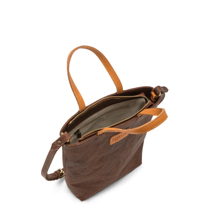 A washable paper tote bag is shown from a top down angle. It features two top handles, a long shoulder strap, a top zip closure and an inside zip pocket. It is chocolate brown in colour.