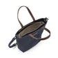 A washable paper tote bag is shown from a top down angle. It features two top handles, a long shoulder strap, a top zip closure and an inside zip pocket. It is navy in colour.