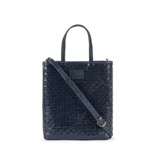 A woven washable paper tote bag is shown from the front angle. It has two top handles and a long shoulder strap. It is navy in colour.