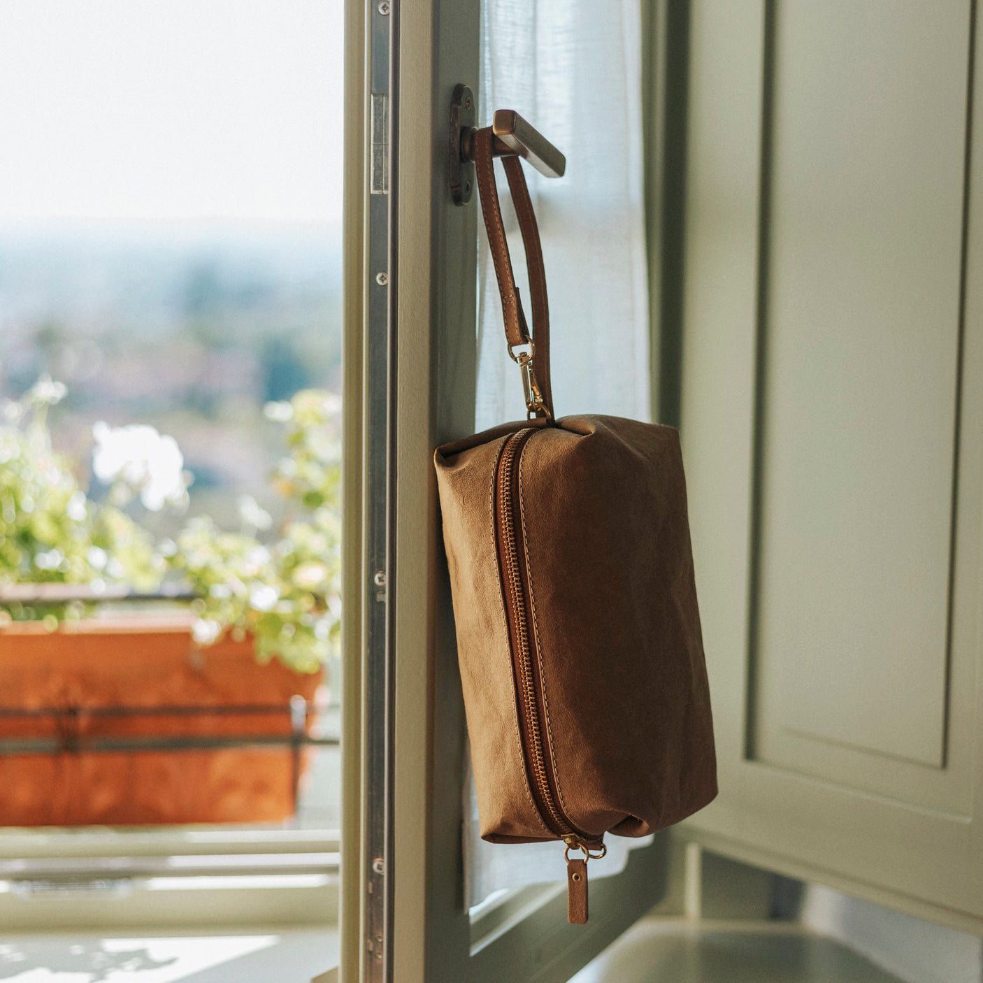 A washable paper pouch, tan in colour, is shown hanging from a window by its handle.