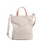 A washable paper tote bag is shown from the front angle. It has a relaxed shape, two top handles and a long shoulder strap. It is pale grey in colour.