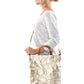 A blonde woman is shown from the side wearing casual clothing. She wears a crossbody washable paper tote bag with top handles. It is metallic gold in colour.
