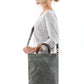 A blonde woman is shown from the side wearing casual clothing. She wears a crossbody washable paper tote bag with top handles. It is dark grey in colour.