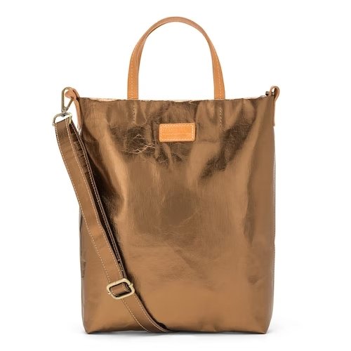 A washable paper tote bag is shown from the front angle. It has a relaxed shape, two top handles and a long shoulder strap. It is metallic bronze in colour.