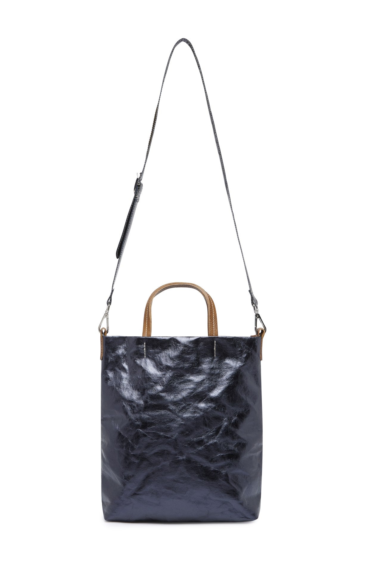 A washable paper tote is shown with a long shoulder strap pointing skywards. It has two top handles and is metallic navy in colour.