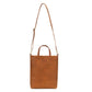 A washable paper tote is shown with a long shoulder strap pointing skywards. It has two top handles and is rich tan in colour.