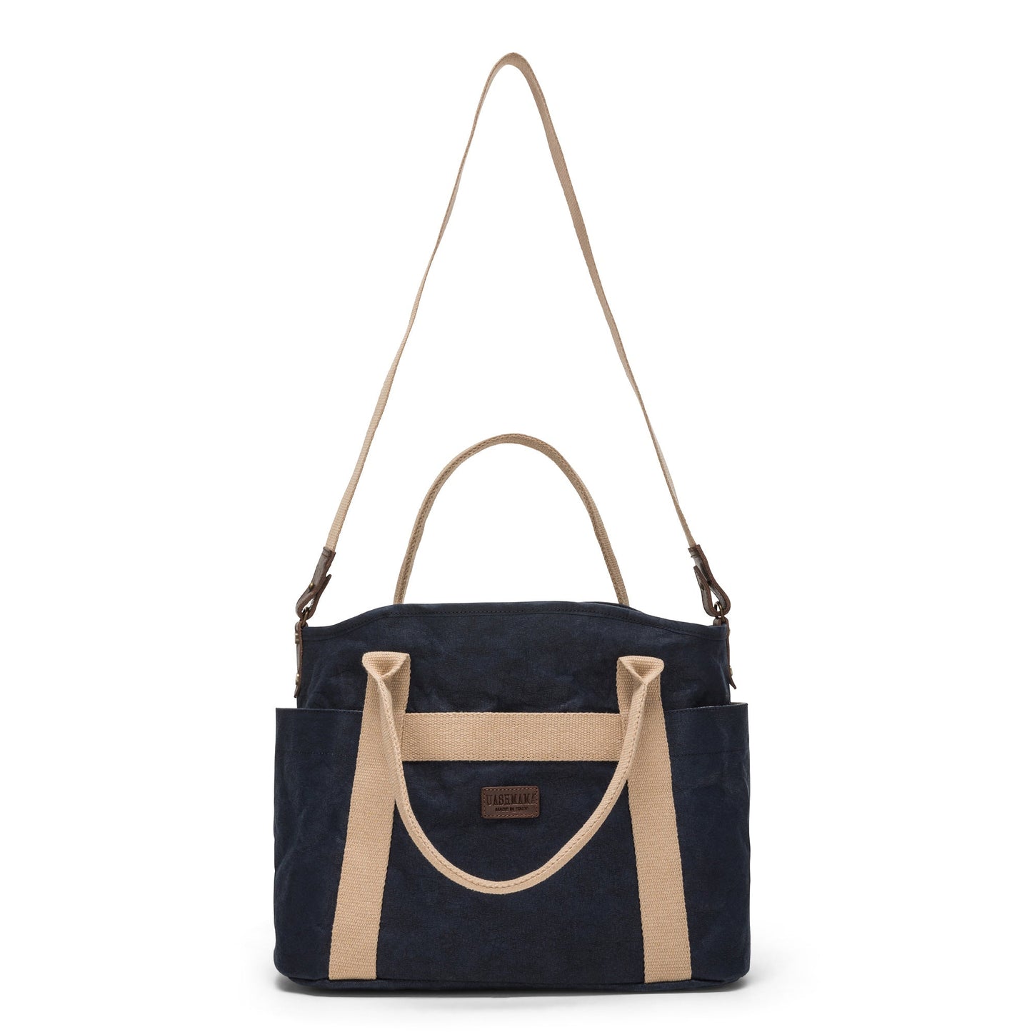 A large washable paper shopper bag is shown from a front angle. It features a long canvas shoulder strap and two top handles. It has an external pocket running the length of the bag, and the UASHMAMA logo stamped in the front. It is shown in a navy colour.