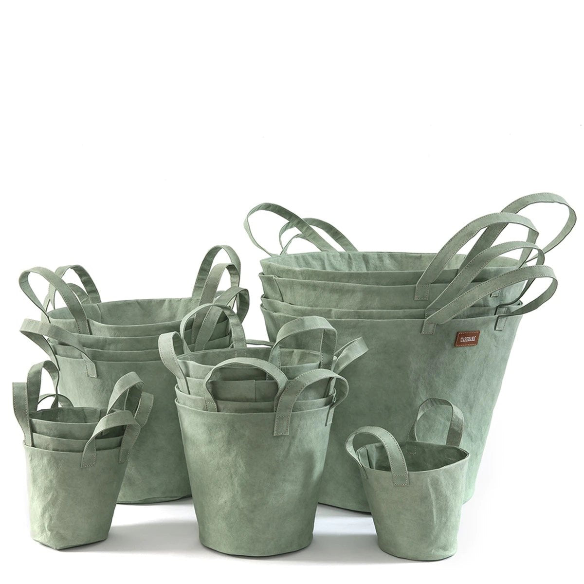 A selection of washable paper baskets are shown stacked in one another, in four varying sizes. They are shown in a sage green colour.