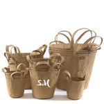 A selection of washable paper baskets are shown stacked in one another, in four varying sizes. They are shown in a sand colour, and the basket in the middle is labelled "SM."