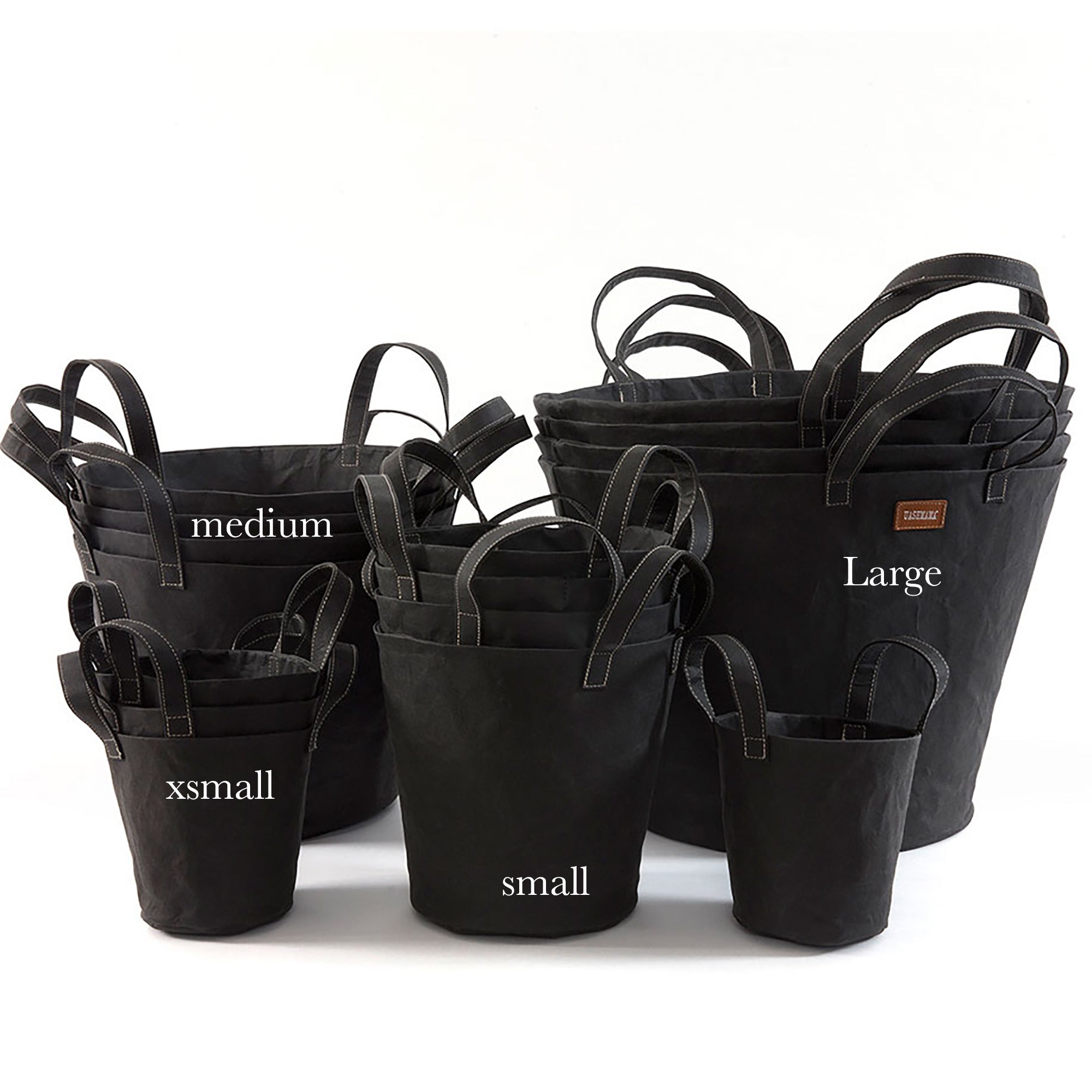 A selection of washable paper baskets are shown stacked in one another, in four varying sizes. They are shown in a black colour. They are labelled xmall, small, medium and large.