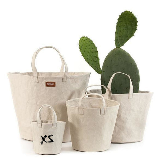 Four individual washable paper baskets are shown in varying sizes. The one at right contains a large cactus, and they are shown in a cream colour. The basket in the front is labelled "XS."