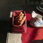 A table top shows a red washable paper tray containing sliced bread. A porcelain jug sits at right on top of a washable paper table runner.