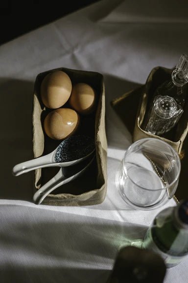 A washable paper tray sits on a white table cloth. It contains delicate spoons and eggs.