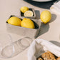 Two washable paper trays in varying sizes hold lemons, they are both shown in a grey colour.