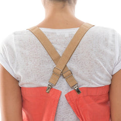 A woman is shown wearing a white t-shirt, from the back. She wears a watermelon coloured washable paper apron with crossed washable paper straps in tan. 