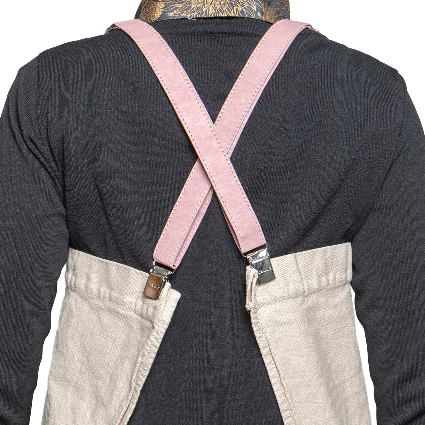 A person is shown from the back wearing a black long-sleeved t-shirt and a washable paper apron with washable paper and metal clip straps. The apron is beige in colour with pink straps.