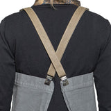 A person is shown from the back wearing a black long-sleeved t-shirt and a washable paper apron with washable paper and metal clip straps. The apron is grey in colour with beige straps