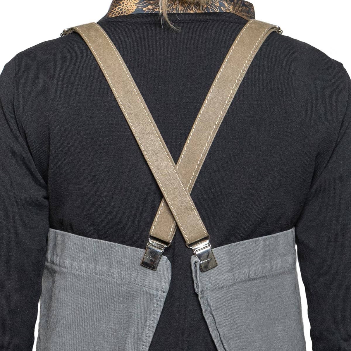 A person is shown from the back wearing a black long-sleeved t-shirt and a washable paper apron with washable paper and metal clip straps. The apron is grey in colour with beige straps