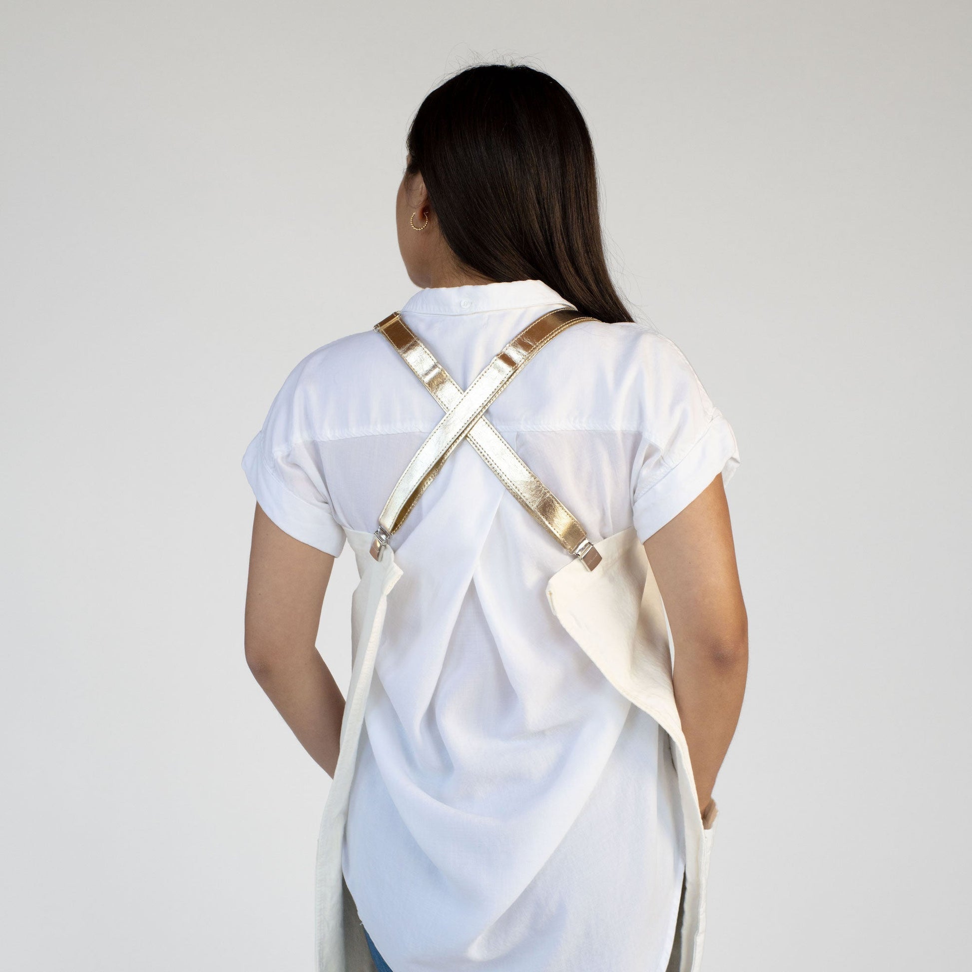 A woman is shown from the back wearing a white shirt and a washable paper apron. The apron is cream in colour, with gold metallic washable paper straps. 