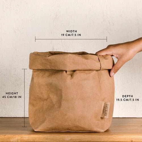 A washable paper bag is shown. The bag is rolled down at the top and features a UASHMAMA logo label on the bottom left corner. The bag pictured is the large plus size in tan. The dimensions are shown on the image and a hand is holding the top right corner of the bag.