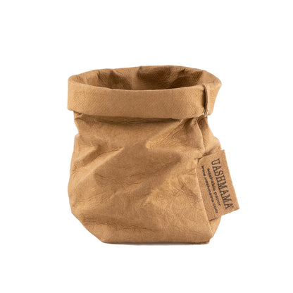 A washable paper bag is shown. The bag is rolled down at the top and features a UASHMAMA logo label on the bottom left corner. The bag pictured is the extra small size in tan.