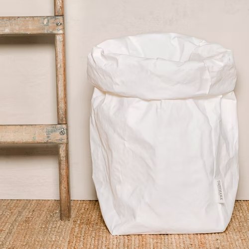 A washable paper bag is shown. The bag is rolled down at the top and features a UASHMAMA logo label on the bottom left corner. The bag pictured is the extra extra large size in white. Next to the paper bag is a wooden ladder.