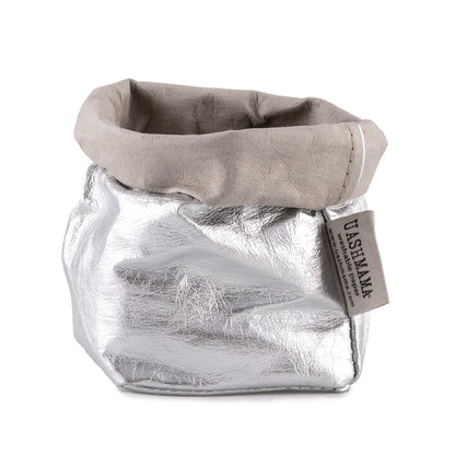 A washable paper bag is shown. The bag is rolled down at the top and features a UASHMAMA logo label on the bottom left corner. The bag pictured is the piccolo size in metallic silver.
