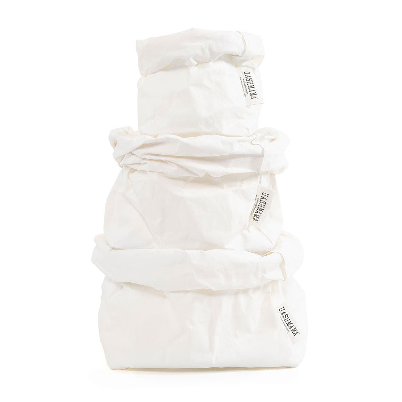 A stack of white washable paper bags in three sizes with large on the bottom, medium in the middle and small on top.