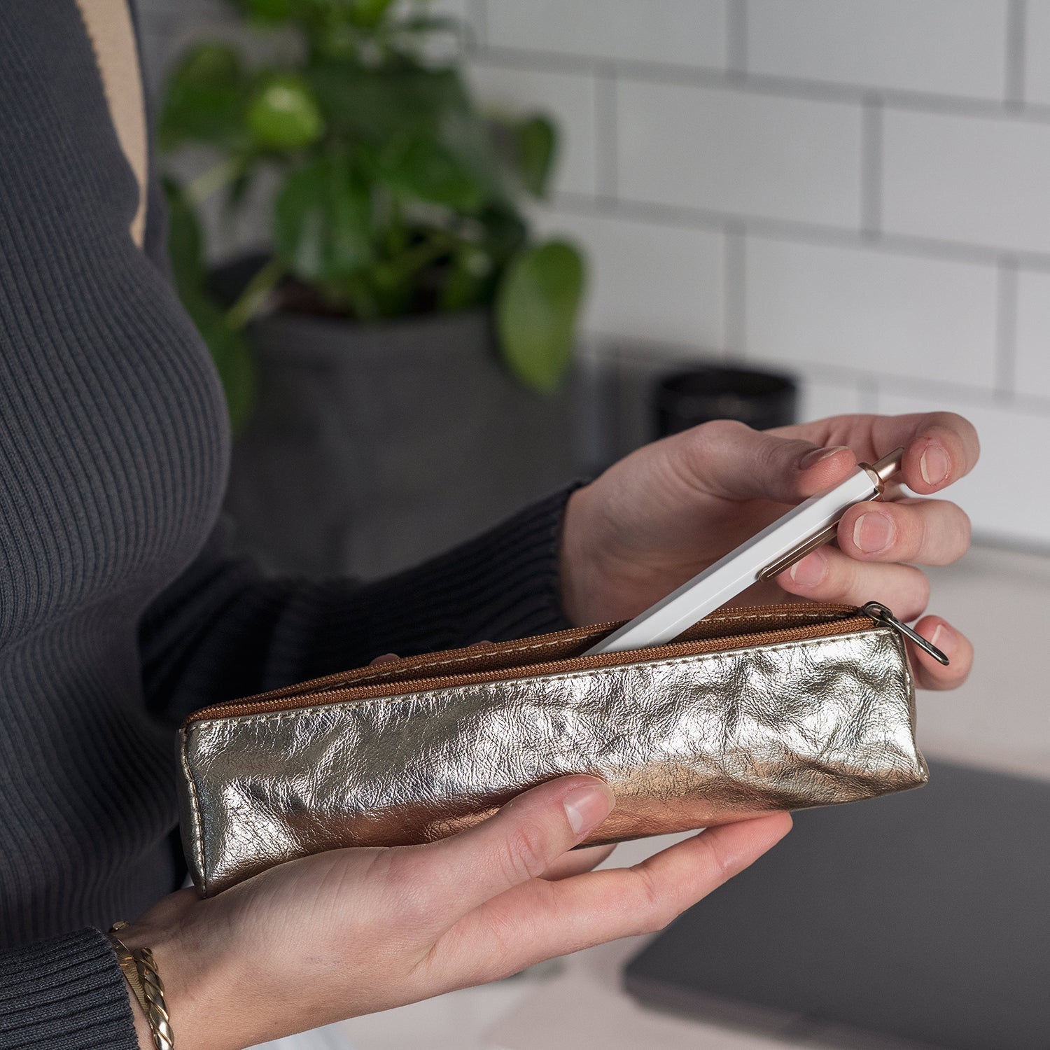 A woman is showing putting a pen into a metallic platinum washable paper pencil case. 