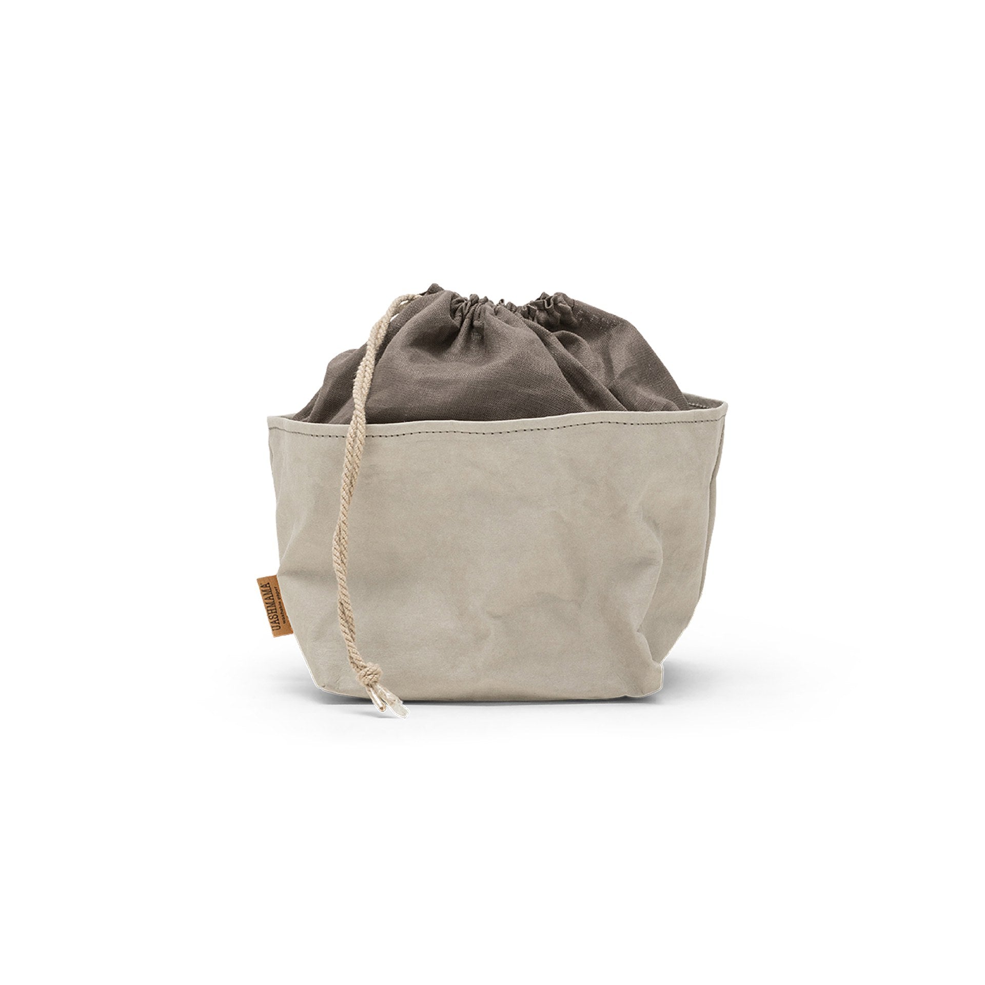 A washable paper bread bag with a drawstring organic linen top is shown. The bag has a small UASHMAMA logo label on the left hand side and fastens with a beige cord drawstring. The bag is pale grey in colour with a dark grey linen drawstring top.