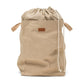 A washable paper laundry bag with a drawstring linen top is shown. The bag has two small recycled cotton handles on either side at the top of the bag, and one drawstring closure at the top. A small leather UASHMAMA logo leather label is on the front of the bag. The bag is sand in colour.