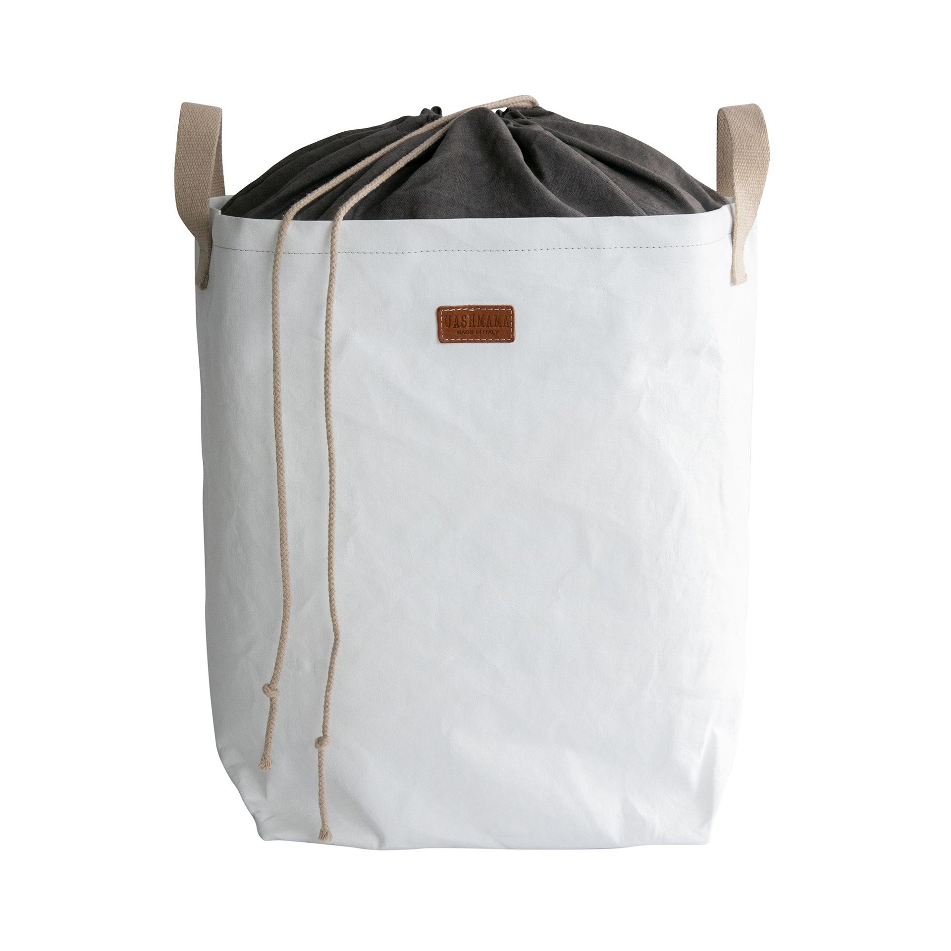 A washable paper laundry bag with a drawstring linen top is shown. The bag has two small recycled cotton handles on either side at the top of the bag, and one drawstring closure at the top. A small leather UASHMAMA logo leather label is on the front of the bag. The bag is white in colour with a dark grey linen drawstring top.