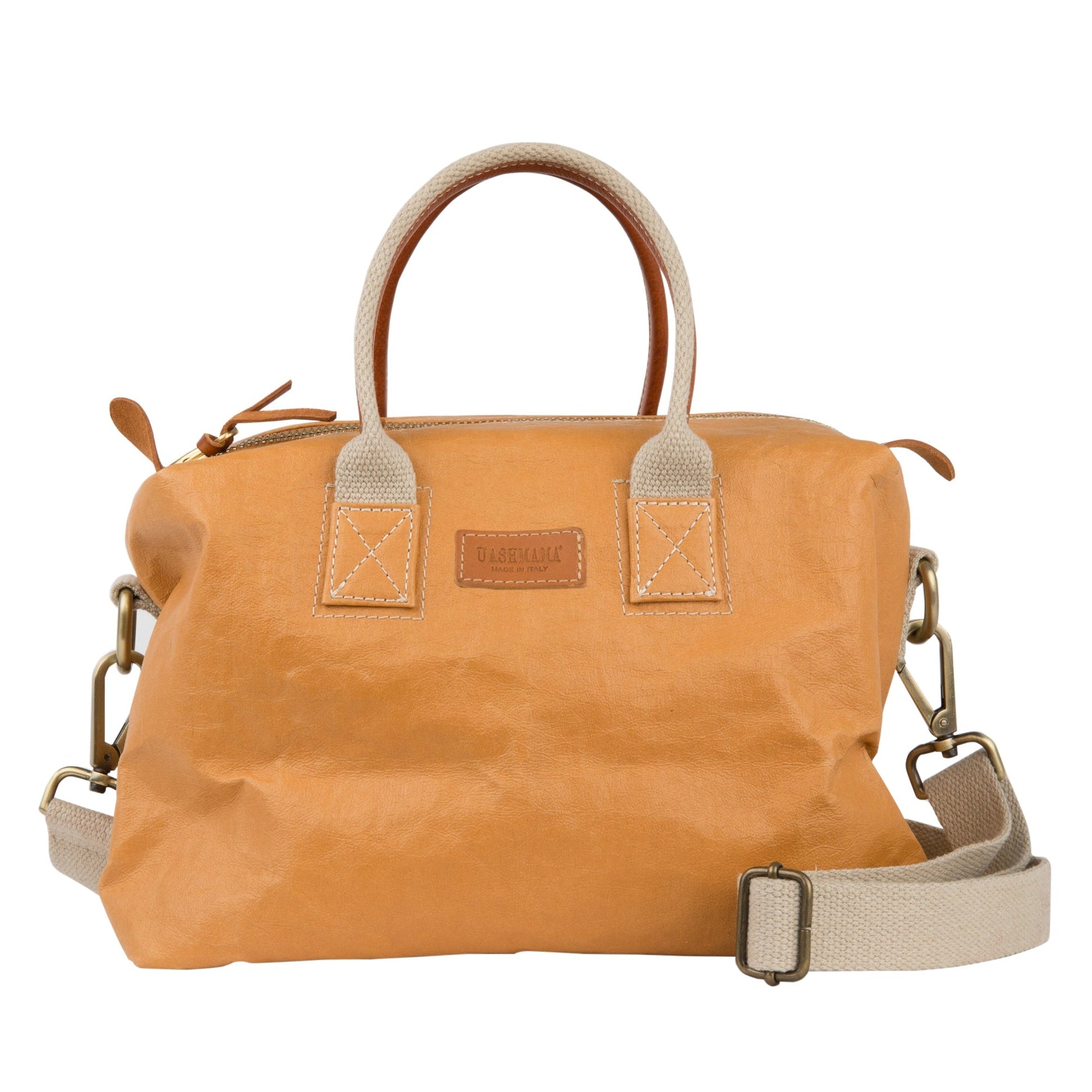 A washable paper holdall with two short carry handles and one long recycled cotton strap. The holdall closes with a zip which has leather zip pulls. The holdall has leather details attaching the straps to the bag and a small UASHMAMA leather logo label. The bag shown is tan with tan leather details. The holdall is the small size.