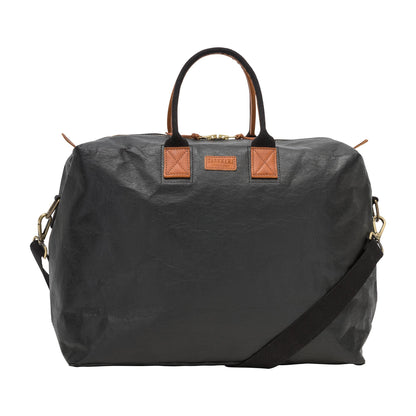 A washable paper holdall with two short carry handles and one long fabric strap. The holdall closes with a zip which has leather zip pulls. The holdall has leather details attaching the straps to the bag and a small UASHMAMA leather logo label. The bag shown is black with tan leather details. The holdall is extra large in size.